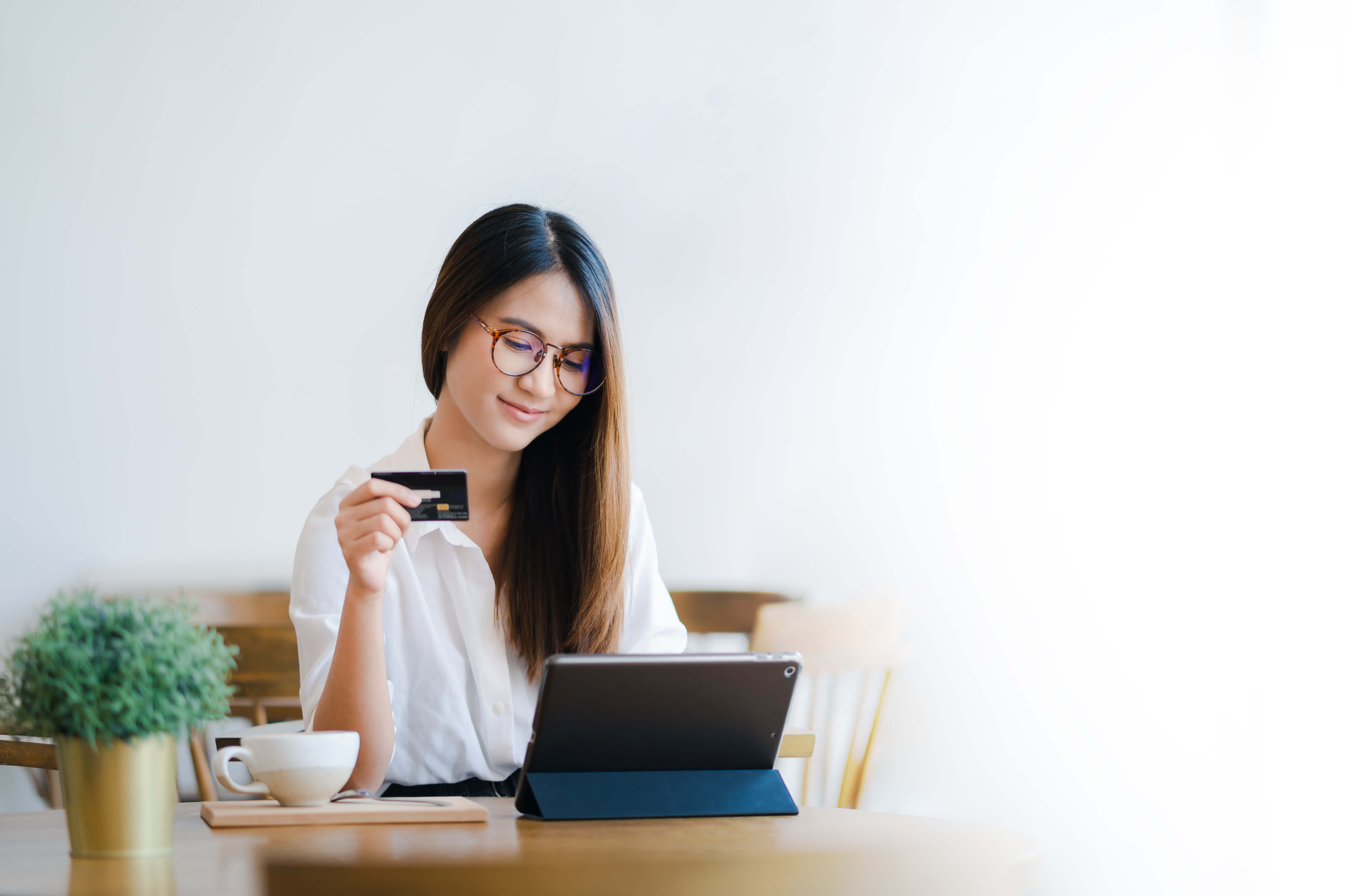 A young woman holding a credit card in her hand while shopping on her iPad