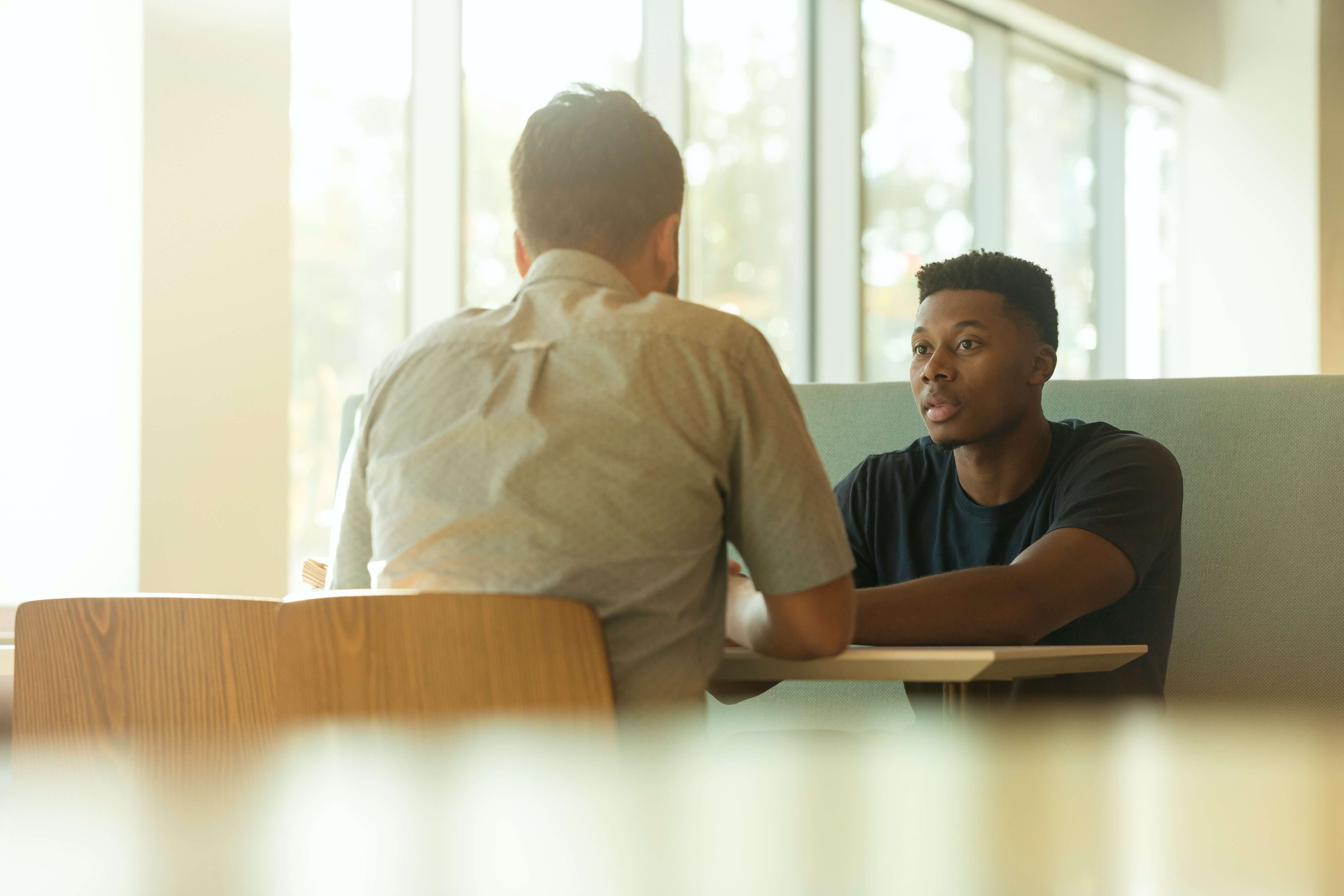 Two young men sitting on a table and talking to each other